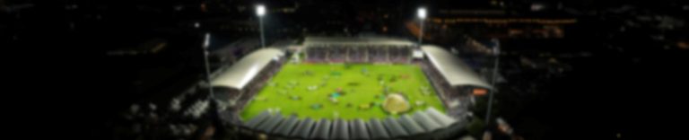 Eine unscharfe Drohnenaufnahme eines großen Stadions bei Nacht mit Hindernissen auf dem Rasen.